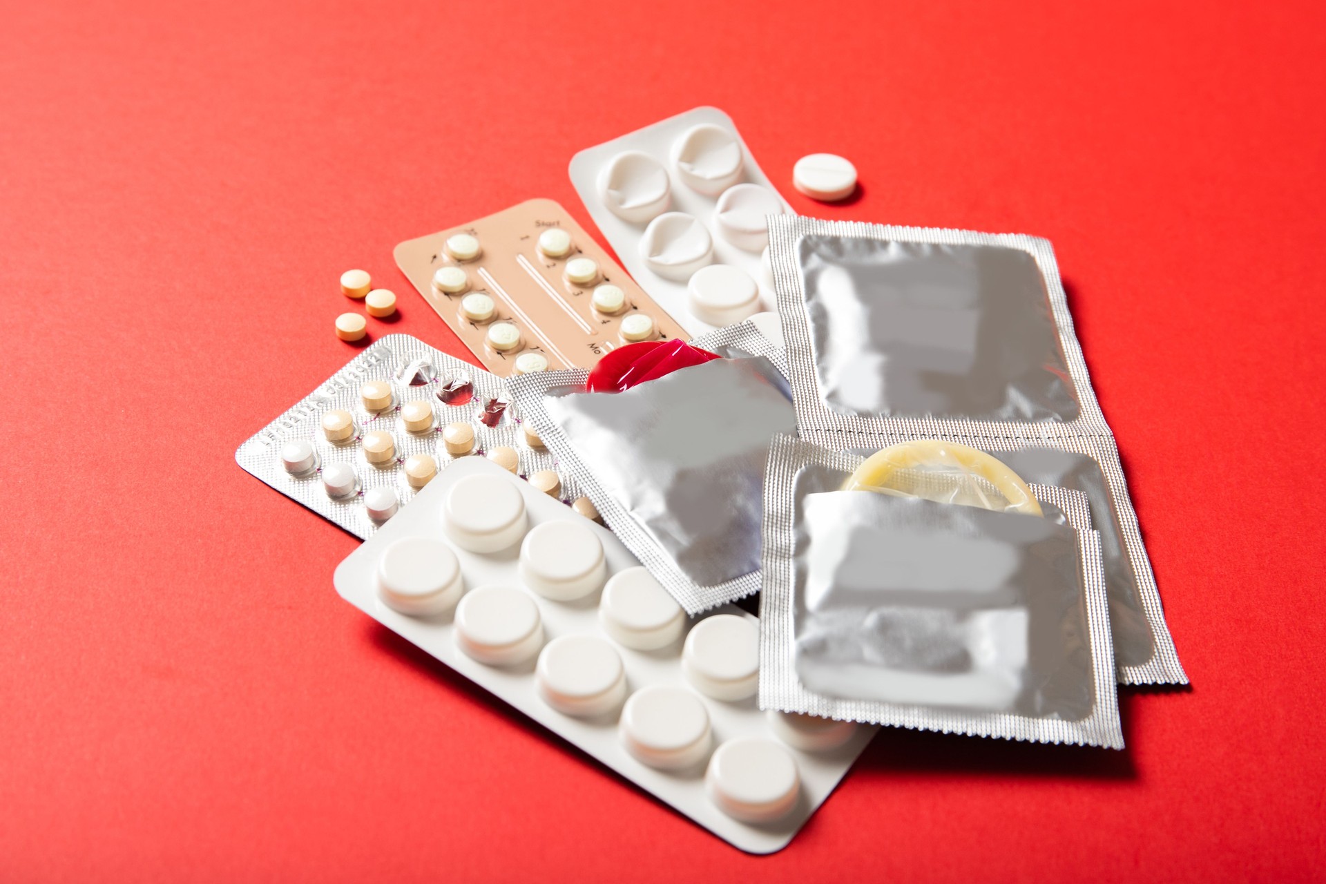 Birth control pills and condoms on a red background. Close-up