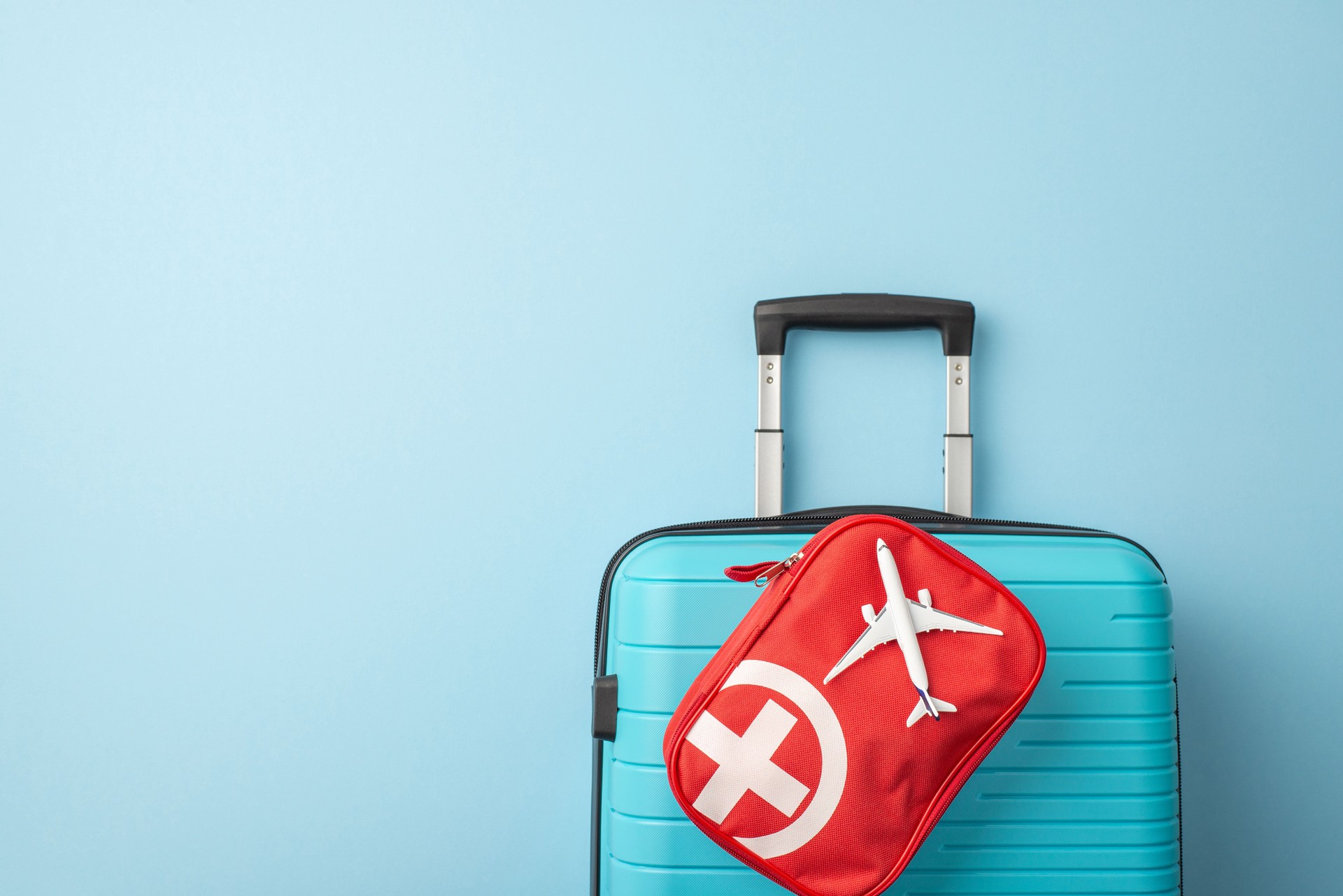 A symmetrical image of a blue suitcase is complemented by a red travel emergency kit. Travel essentials are organized on a minimal blue background